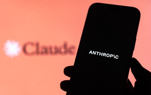 A hand holds a smartphone reading "Anthropic" in front of the Claude logo.