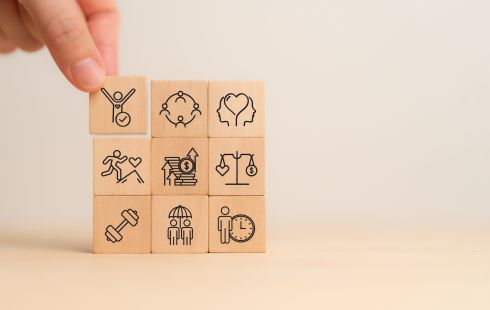 A photo of a hand with wooden blocks with physical, mental and emotional health icons to show the idea of employee wellbeing. 