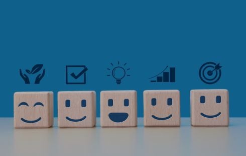 An image of wooden blocks with smiling faces and icons to show the idea of employee wellbeing. 