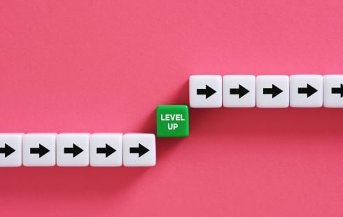 Blocks with arrows and the words “level up” on a pink background show the idea of professional development at work. 