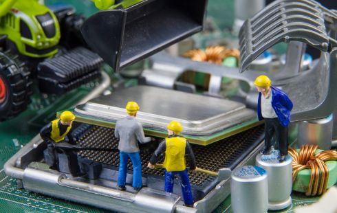 A photo of miniature construction figures working on a motherboard to show the idea of an engineering team building software. 