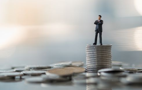 A photo of a miniature figure on a stack of coins to show the idea working in a financial department at a tech company.