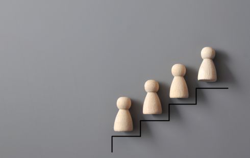 A series of wooden figures are posed on a drawing of steps to show the idea of employee career growth.