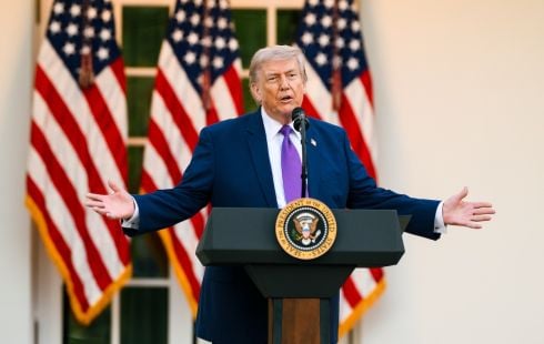 President Trump stands behind a podium, with three U.S. flags standing behind him.