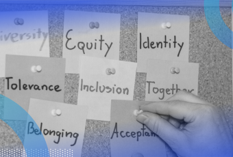 A close-up of a corkboard with sticky notes reading diversity, equity, identity, tolerance, inclusion, together, belonging and acceptance pinned to it. A person’s hand is actively pinning the acceptance note to the board.