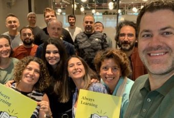 Udemy employees pose for a group selfie holding signs that read “Always Learning.”