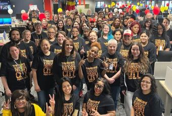 A large group of TrueML employees post in an office wearing matching shirts and surrounded by balloons.