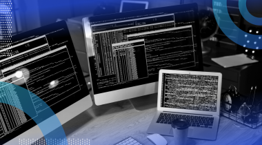 Two large screens, a laptop, and a to-go cup of coffee sit on a desk, displaying many commands in text boxes. /software-engineering-perspectives/programming-jobs-recession