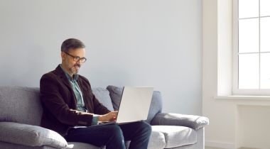 A man is on a couch doing work on a laptop.