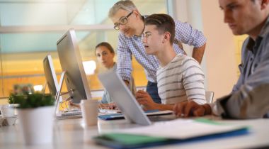A mentor and apprentice work together at a desktop computer.