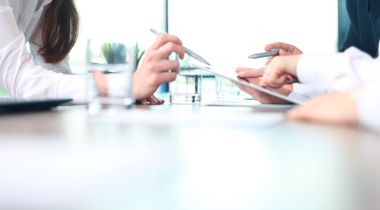 A consultant points to a tablet as they advise a client.