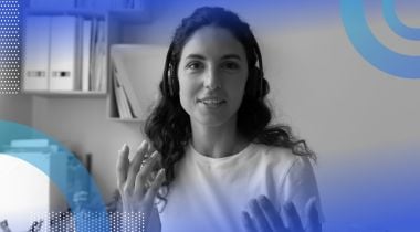 A young woman wearing headphones is watching a computer screen and making hand gestures.