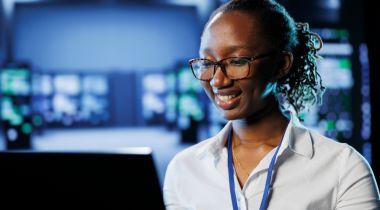 An IT professional smiles at a computer monitor.