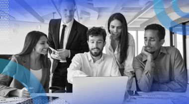 Five coworkers crowded around a laptop looking at the screen with varying levels of interest.