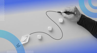 A close-up of someone’s hand drawing a curved line for a paper boat to follow around blocks in its path.