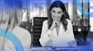 A woman is smiling and looking at a sheet of paper, and another woman sits across from her.