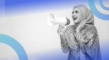 A woman in a headscarf playfully shouting into a microphone toward the side.