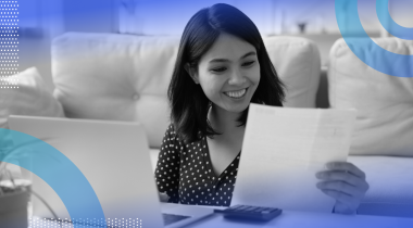 A smiling woman is looking at a paper pay stub.