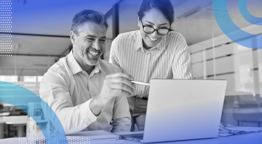 A man and a woman are looking at a computer screen and are smiling.