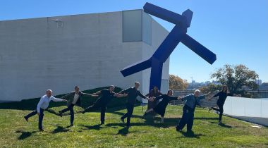 The Nisos executive leadership team stands on the lawn of the Kennedy Center for the Performing Arts in Washington, D.C., in front of “Blue,” a blue geometric modern art statue by Joel Shapiro.  