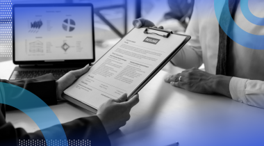 A recruiter looks at a resume on a clipboard as a candidate in a tie sits across the table