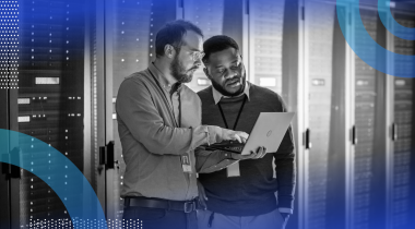 Two database managers reviewing information on a laptop in a server room