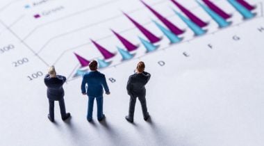 Three miniature figures representing sales leaders stand on a piece of paper with a chart, looking away from the camera.