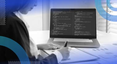 A developer works on a laptop full of code and writes in a notebook