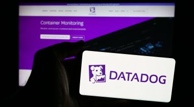 The Datadog logo on an iPhone with a computer screen in the background showing the Datadog website