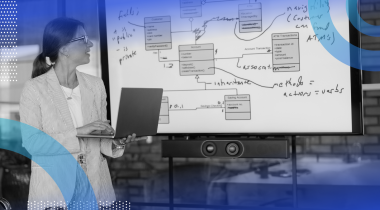 A woman presents with a laptop in front of a whiteboard