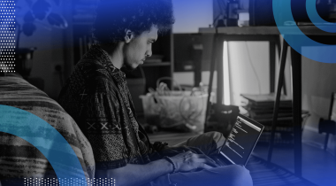 A developer works on a laptop next to a bed