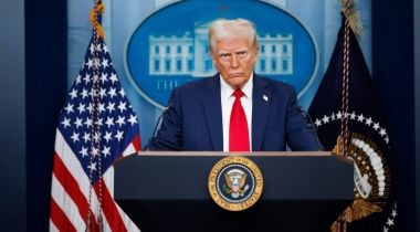 Image of Trump standing behind a podium, with an American flag in the background.