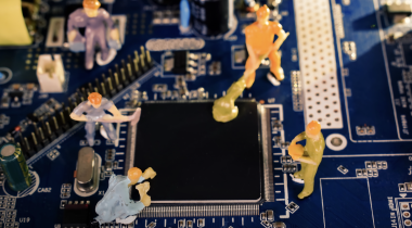 A photo of miniature figures working on a computer motherboard to show the idea of engineers working on AI.