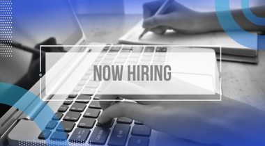 A closeup on hands typing on a laptop keyboard with a Now Hiring sign atop