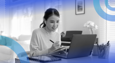 A young woman works on a laptop and writes in a notepad