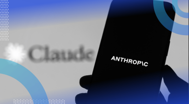 A hand holds a smartphone with the Anthropic logo in front of a screen advertising the company's Claude tool.