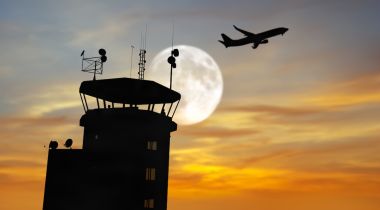 An airpline flies over a Terminal Radar Approach Control (TRACON) tower.
