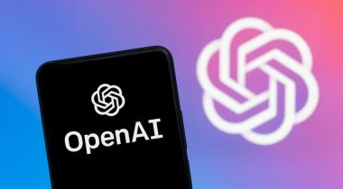 A smartphone with the OpenAI logo is pictured in front of a larger image with the OpenAI logo.