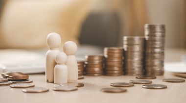 Three wooden figures next to piles of coins to show the idea of competitive compensation and holistic perks that support work-life balance for Academia.edu employees. 