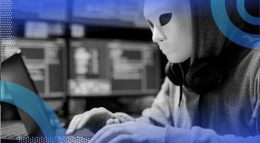 A scammer wears a mask and works on a laptop