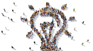 An illustration of people standing in the shape of a lightbulb to show the idea of working together on tech that impacts people and new ideas. 