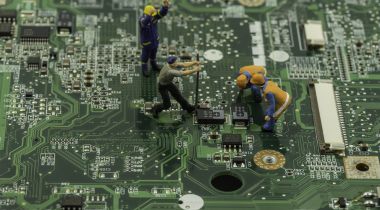 Miniature figures work on a motherboard to show the idea of product teams building a piece of technology.