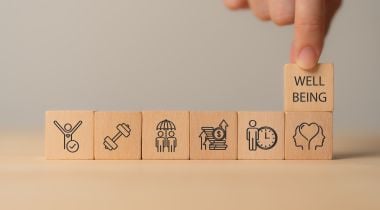 A photo of wooden blocks with physical, mental and emotional health icons to show the idea of employee wellbeing.