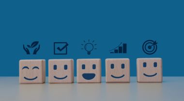 An image of wooden blocks with smiling faces and icons to show the idea of employee wellbeing. 