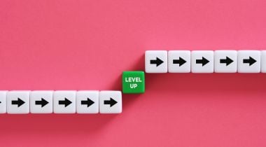 Blocks with arrows and the words “level up” on a pink background show the idea of professional development at work. 