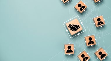 A photo of wooden blocks with icons of a hand shake and people connected by white lines to show the idea of a cross functional and collaborative customer success team. 