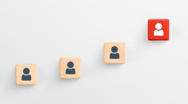 Wooden blocks with icons of people in an ascending pattern with a red one at the top to show the idea of upward career growth. 