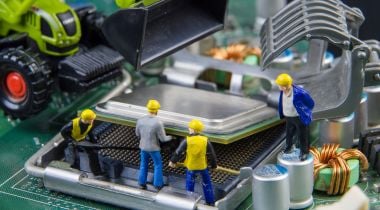 A photo of miniature construction figures working on a motherboard to show the idea of an engineering team building software. 