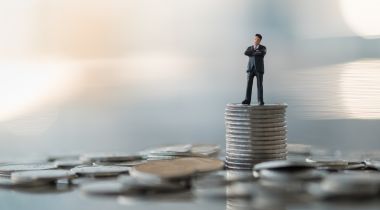 A photo of a miniature figure on a stack of coins to show the idea working in a financial department at a tech company.