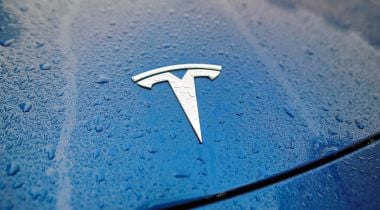A Tesla logo in the front hood of a Tesla vehicle soaked in rain.